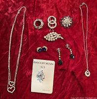 Full lot view showing all pieces arranged on red fabric: two necklaces, three pins, two pairs of earrings, and a barrette.