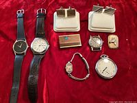 Full lot arranged on red fabric, showing watches, cufflinks, money clip, and scarf ring