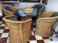 Full view of set showing all four barrel arm wicker chairs with blue cushions around the wicker pedestal table topped with round glass.