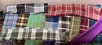 Photo shows a collection of wool scarves in various plaid patterns laid out on a surface.