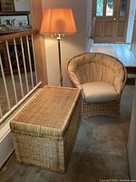 Wicker papason chair with cushions, wicker trunk, and brass floor lamp positioned together.