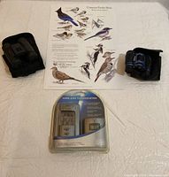 Full lot overview including wireless thermometer packaging, two pairs of binoculars, and bird identification poster on a white surface.