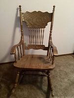 Full front view of wooden rocking chair showing carved backrest, armrests, and spindle legs.