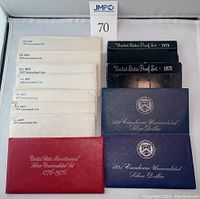 White U.S. Mint envelopes for 1973–1979 uncirculated sets, red Bicentennial folder, blue Eisenhower silver dollar folders, black proof set boxes