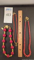 All three necklaces arranged on black background next to ruler showing approximate lengths