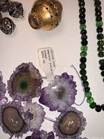 Close-up of four purple amethyst stalactite slices with tag and partial view of gold bead and green and black strands