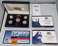 Full overview of the lot showing three coin sets including 24k gold plated set, 2000 and 2002 proof quarter sets, and 2002 uncirculated set in boxes.