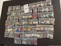 Overview of 56 small resealable bags each containing a pair of earrings arranged in a grid on a black surface