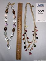 Both necklaces laid flat side by side with ruler for scale and lot tag visible