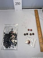 Plastic bag of loose black faceted oval beads and six special beads arranged beside wooden ruler