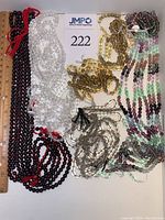 Layout of multiple bead strands showing varied colors including deep red, clear, gold, green, pink, purple, and amber tones, with a measuring ruler for scale.