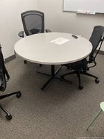 Assembled round table with gray laminate top and black metal base shown with office chairs around it.