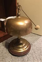 Front view of brass dome gong on pedestal base with striker resting against it