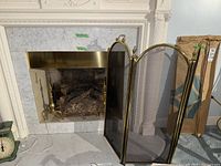 Brass three-panel firescreen with mesh in front of marble fireplace.