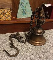 Full view showing bronze bell with Ganesha figure on top, chain and hook on carpet.