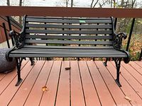 Front view of black cast iron and wood slat bench showing the seat, backrest, and decorative sides