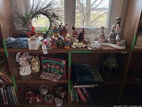 Full view of three shelves filled with various Christmas decorations including wreath, figurines, musical bells box, and tins