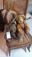 Photo showing two fur bears sitting on a woven wooden chair, one darker fur and one lighter tan fur bear.
