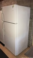 Front and side angled view of white GE Hotpoint refrigerator with top freezer door closed, displaying textured surface and handle design.