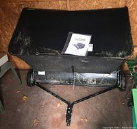 View of front and top of lawn sweeper showing fabric collection bag full width and manual placed on top.