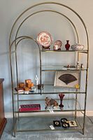 Full front view of the metal and glass etagere shelf with assorted decorative items on the shelves