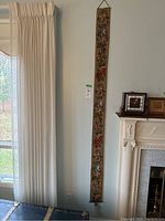 Photo showing the full view of the long narrow tapestry bell pull hanging on the wall near a fireplace, highlighting its length and floral design.