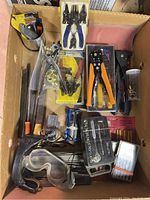 Full top-down view of the assortment of tools laid in a box including pliers, punches, files, screwdrivers, safety glasses, and small hand tools