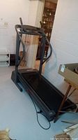 Full view of the black Weslo Space Saver treadmill in basement showing frame, running belt, handles, and control panel.
