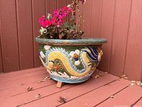 Angled side view of the ceramic planter showing the dragon motif and its colors, with some flowers inside.