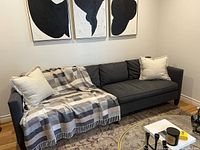 Front view of dark gray low-profile 4-seat sofa with pillows and throw under abstract art