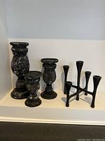Photo showing three black distressed candle holders with varying heights and shapes alongside a modern black metal multi-candle holder.