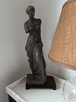 Side view of stone-looking PLA goddess statue placed on white marble table next to a lamp showing texture and missing arms.
