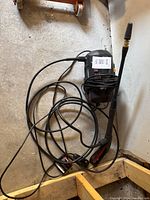 Full view of the electric power sprayer with connected hose and spray wand viewed from above on a concrete floor.