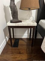Full view of marble top side table next to bed with decorative lamp and statue on top