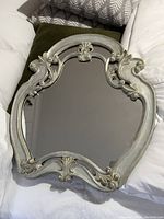 Full view of decorative vintage style wall mirror with ornate distressed frame, laid on fabric surface.