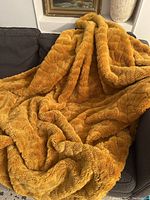 Full view of the mustard yellow plush blanket laid on a dark fabric couch, showing its thick, soft texture and vibrant color.