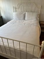 Full queen size bed made with white cotton duvet cover, pillowcases and flat sheet visible on white metal bed frame.