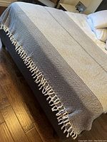 Full view of the queen size blanket laid on a bed showing the entire pattern and tassels on edges.