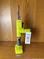 Front view of Ryobi One+ cordless band sander with 1-inch sanding belt, standing upright showing the sanding belt, trigger, and body design.