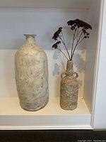 Photo showing both textured vases displayed side by side on a white shelf, highlighting their size difference and textured surfaces.