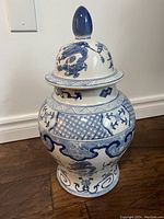 Full view of the blue and white ceramic urn showing dragon and geometric patterns, with the lid on top and blue finial.