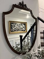 Front view of vintage mirror hanging on wall inside house near staircase and artwork.
