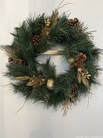 Full view of the larger pine wreath showing green pine needles, pine cones, and gold leaf and berry accents