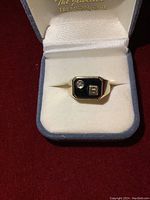 Front view of ring showing round clear gemstone on black enamel top and gold letter B