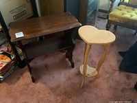 Photo showing dark wood accent table with curved edges next to heart-shaped pine plant stand on carpeted floor.