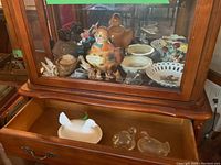 Wide view of novelty dishes including hens on nest dishes, Bunnykins bowl, squirrel lidded dish, beaver cookie jar inside wooden cabinet