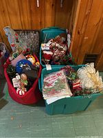 Photo showing two totes filled with various Christmas decorations including a metal lantern, ornaments, greenery, and figurines inside a wooden-paneled room.