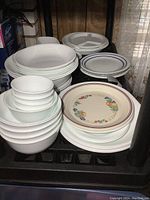 Photo showing stacked white bowls in multiple sizes, nested and arranged, with plates beside them including a floral patterned plate.