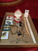 Full view of costume jewelry lot in cardboard tray including necklaces, earrings, brooches, and bracelet.