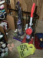 Dyson Ball Animal 2 and Dirt Devil Featherlite upright vacuums placed side by side with a yellow plastic bag containing vacuum accessories in front.